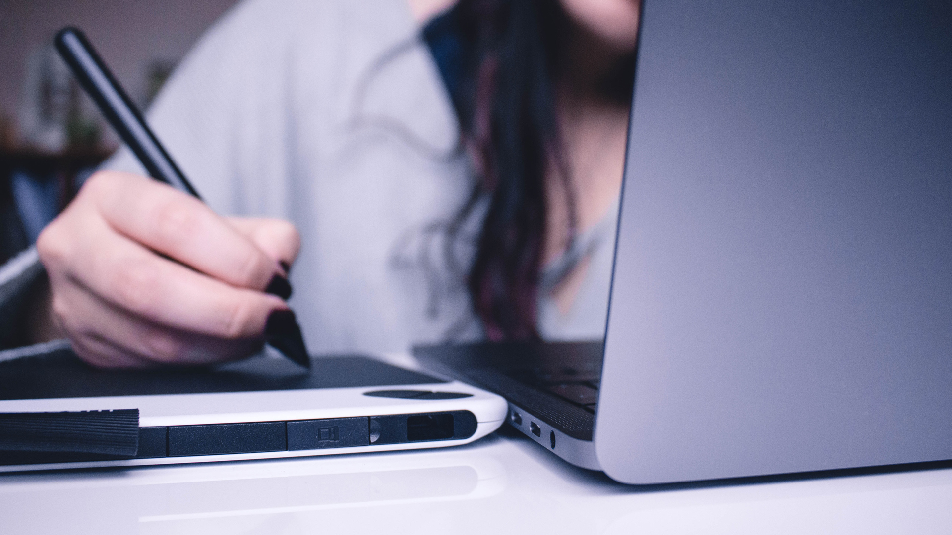 Close up of a woman writing on a notebook next to a laptop